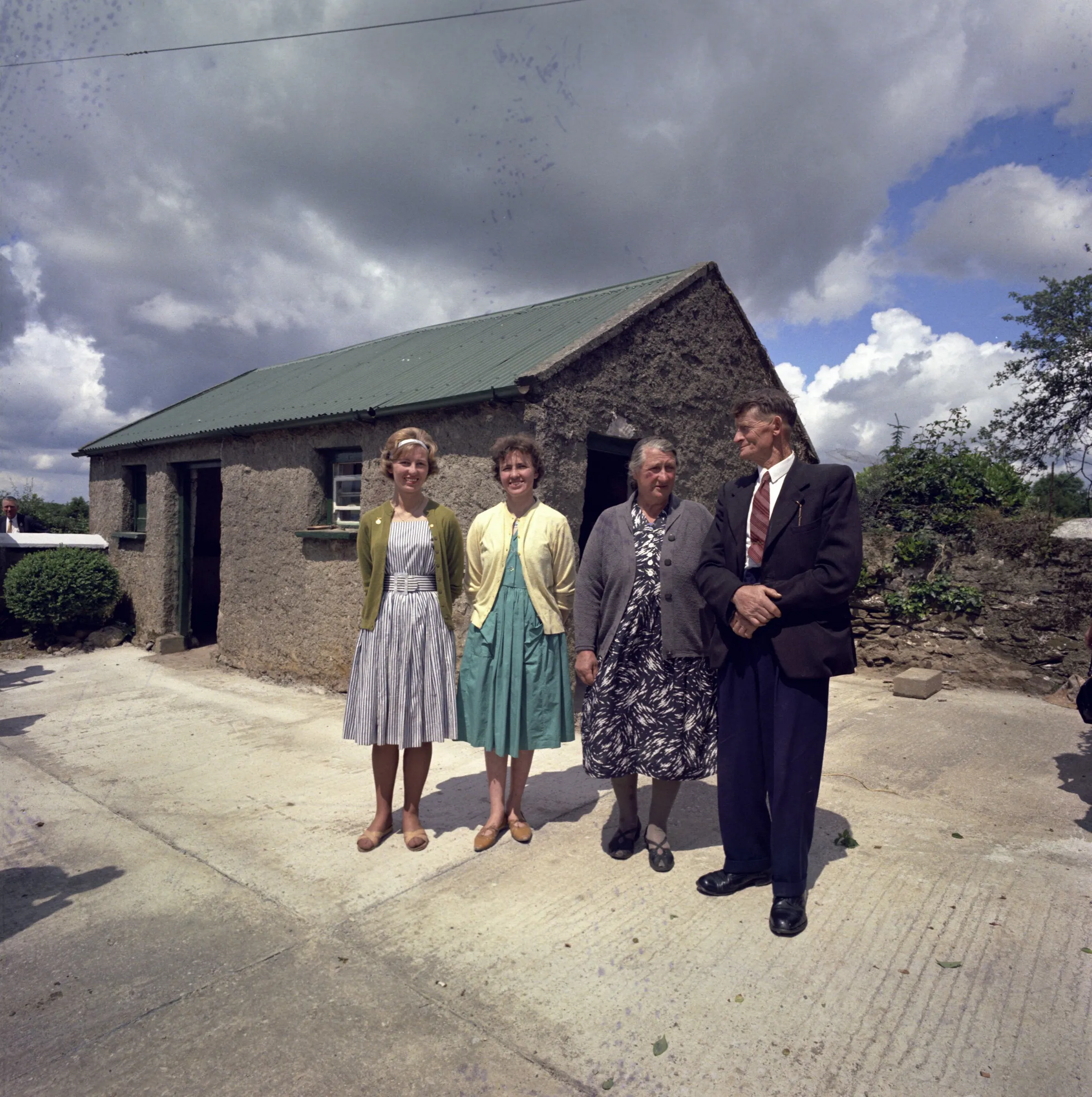 Three women and a man from the Irish Kennedy family stand in the yard outside the old stone cottage with its green corrugated roof.