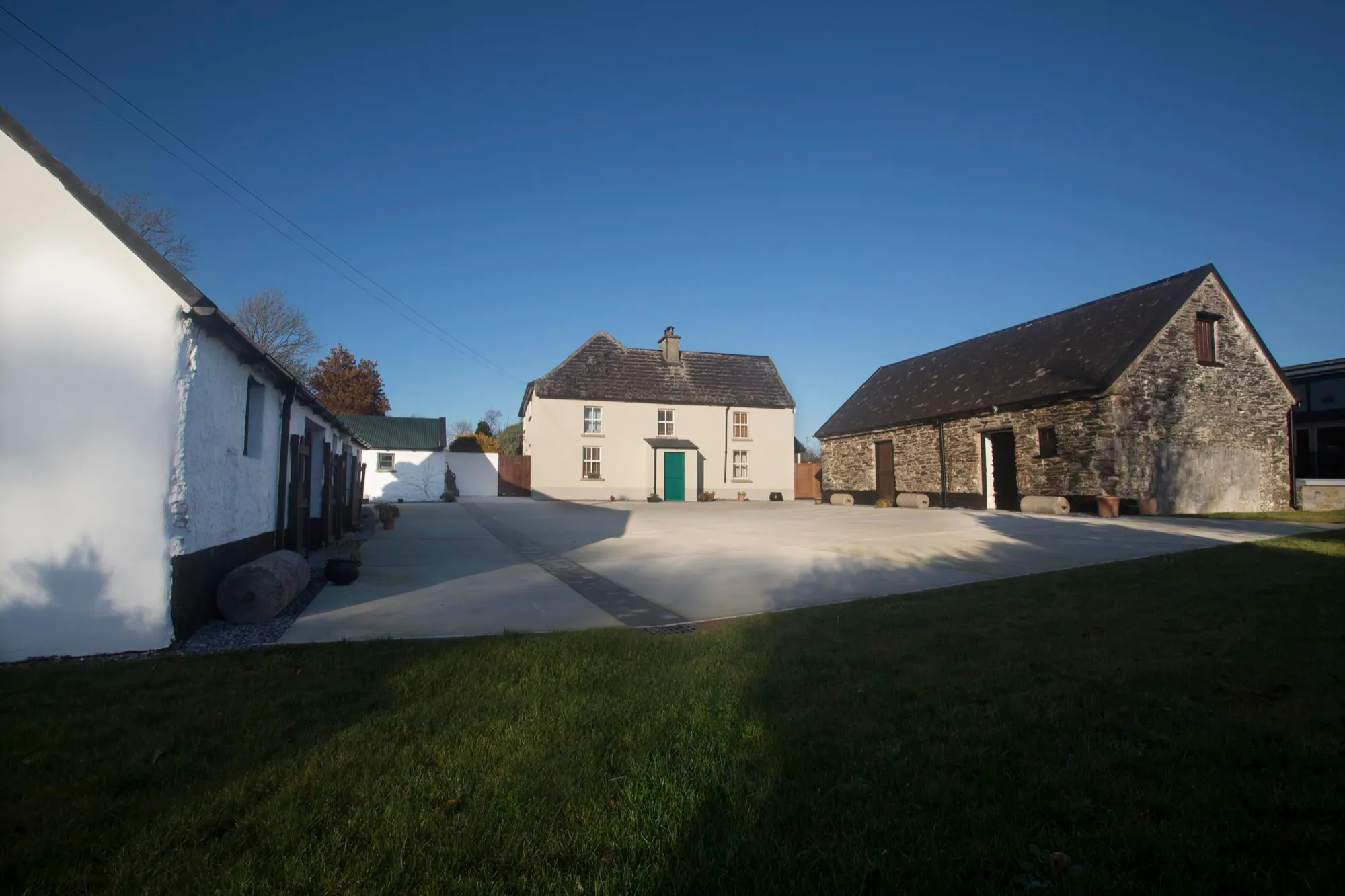 The homestead yard under a clear blue sky: whitewashed and stone farm buildings around a wide yard, with the farmhouse at the far end.